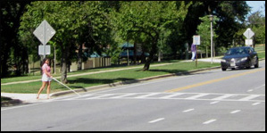 3 photos show the crosswalk; a woman holding a white cane on the ground in front of her walks to the street and puts one foot into the street, with the cane on the ground.